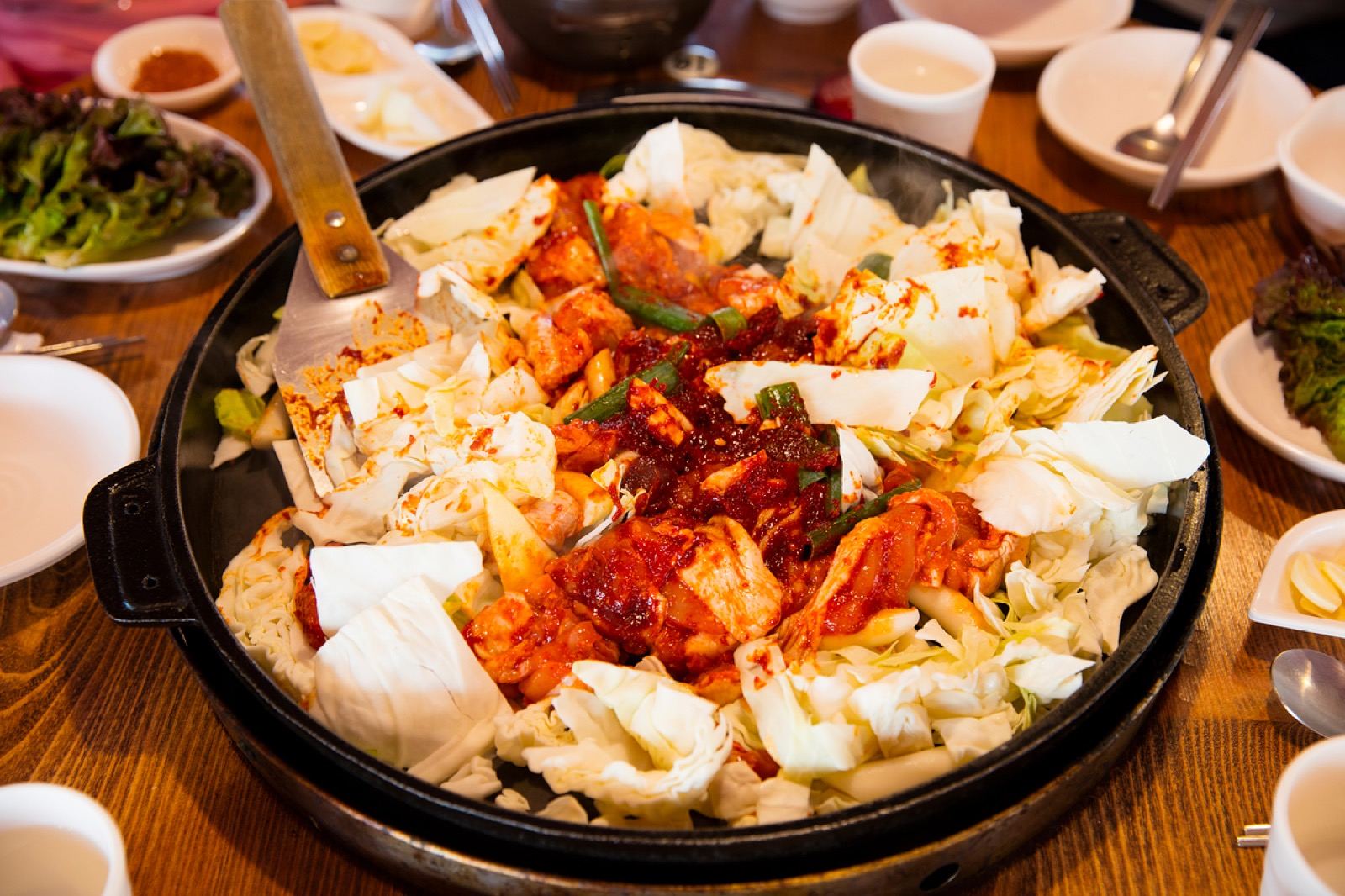 A large iron pan of raw gochujang-marinated dakgalbi with cabbage and rice cake, ready to cook at a Chuncheon restaurant