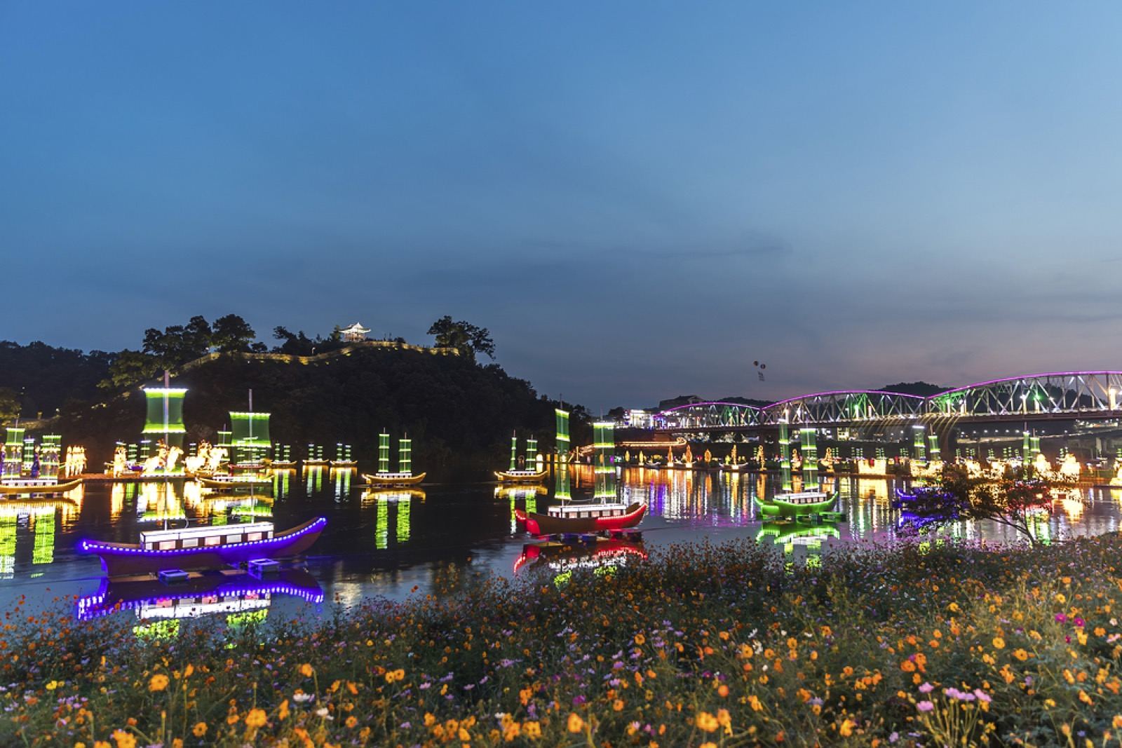 The Geumgang river in Gongju at dusk during the Baekje cultural festival, lit floating lanterns and boats below the fortress hill