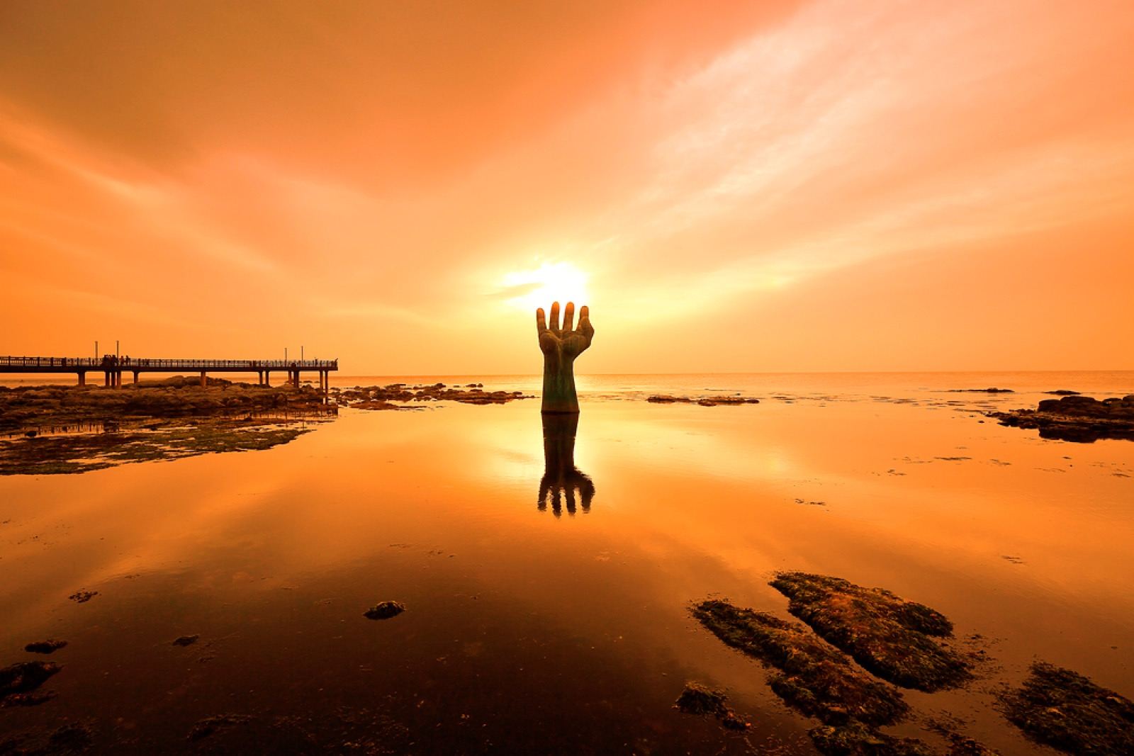 The Hands of Harmony sculpture, a giant bronze hand rising from the sea at Homigot at sunrise
