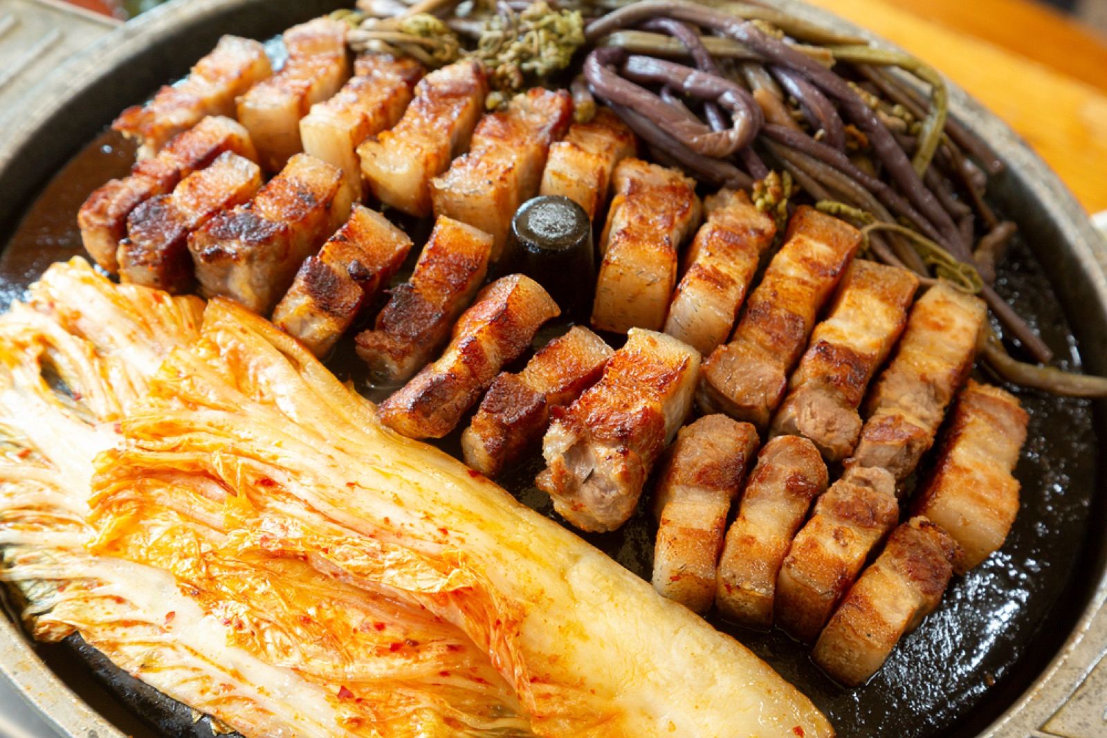 A sizzling platter of grilled Jeju black pork belly served with kimchi and mountain vegetables