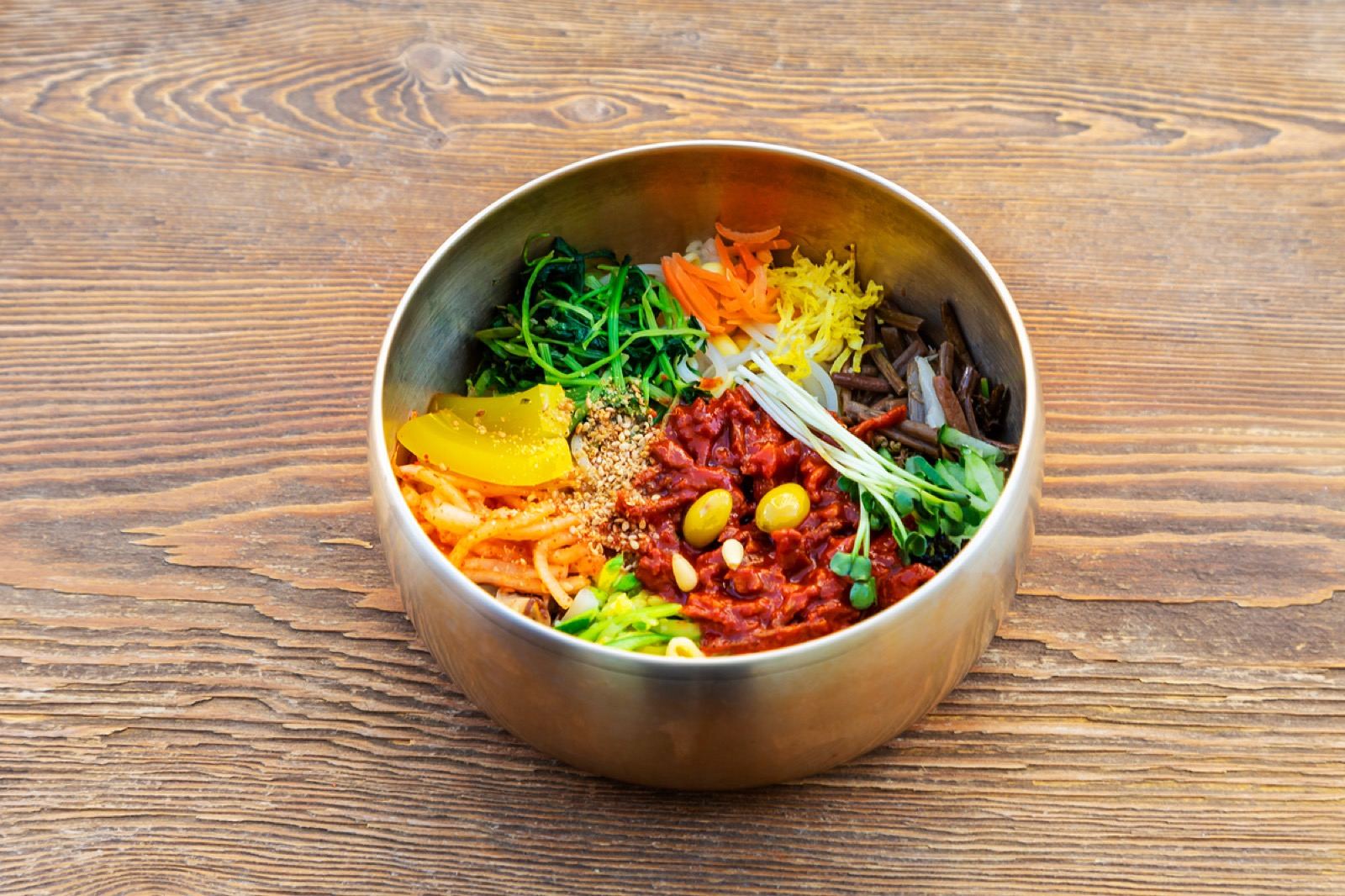 A brass bowl of Jeonju bibimbap topped with seasoned vegetables and a raw egg