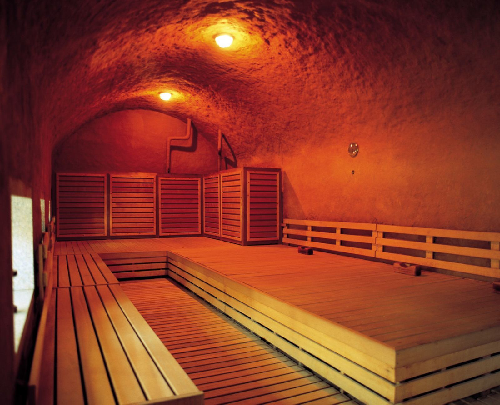 A warm wood-lined themed sauna room in a Korean jjimjilbang, glowing under low kiln-style lighting