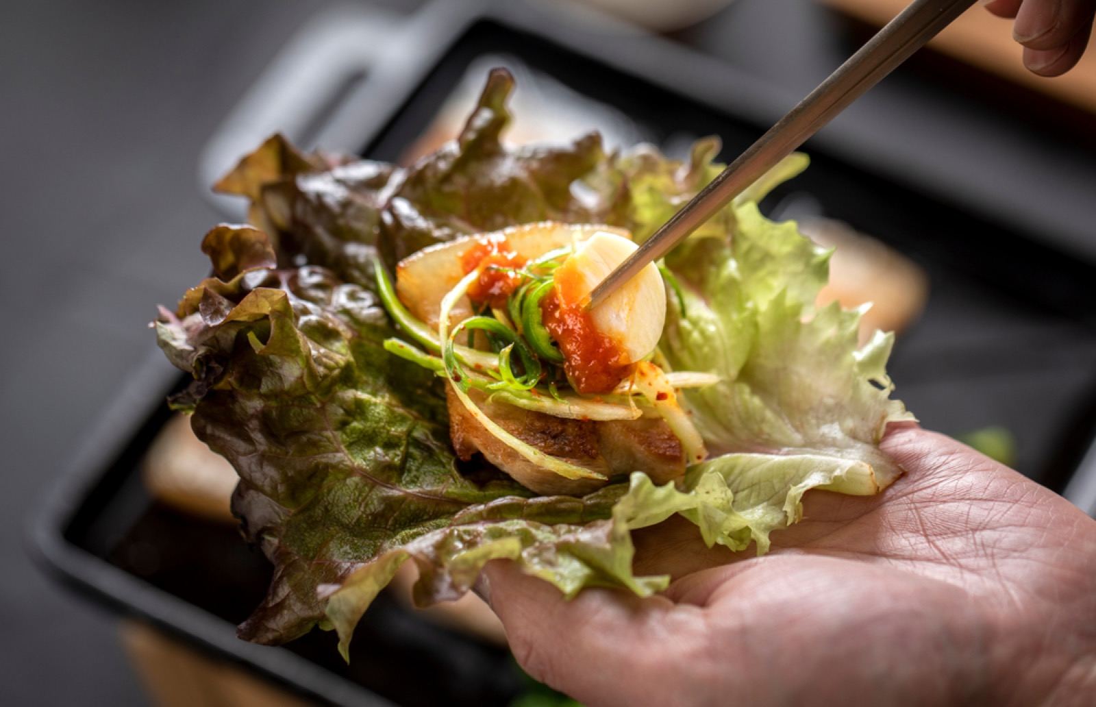 Hands wrapping grilled pork and garnishes in a lettuce leaf